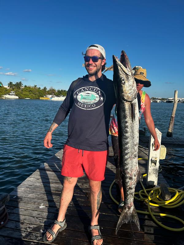 Angler holding a 55-inch barracuda after offshore fishing trip in Cancun